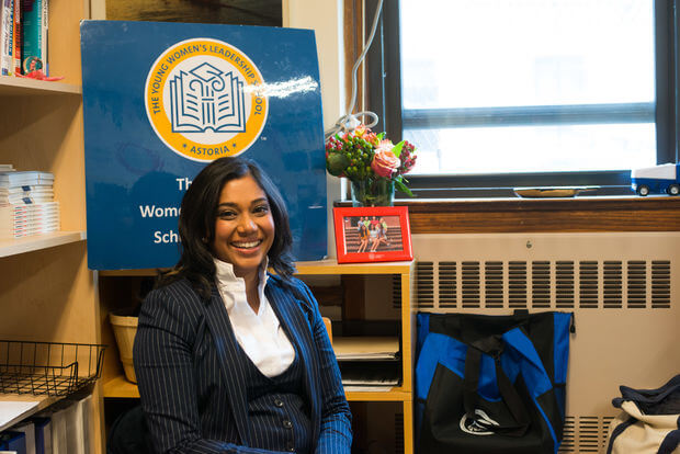 Dr. Allison Persad sits in front of a banner with the TYWLS school crest.