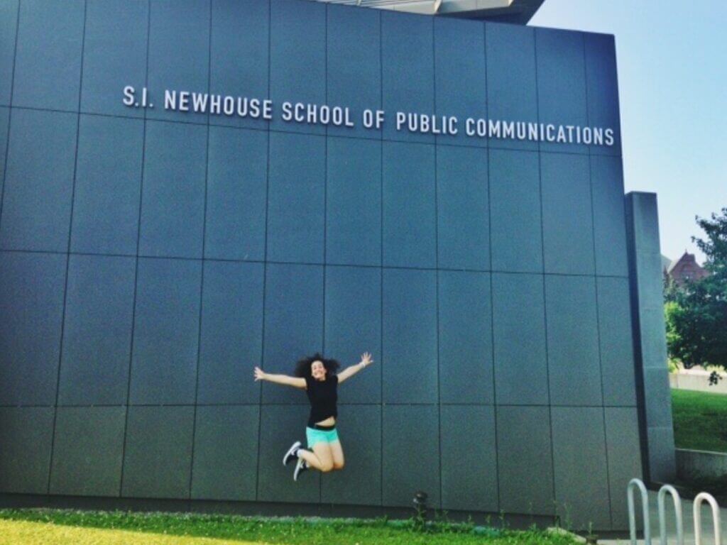 Nicole is jumping in the air in front of the school of public communications where she studied.