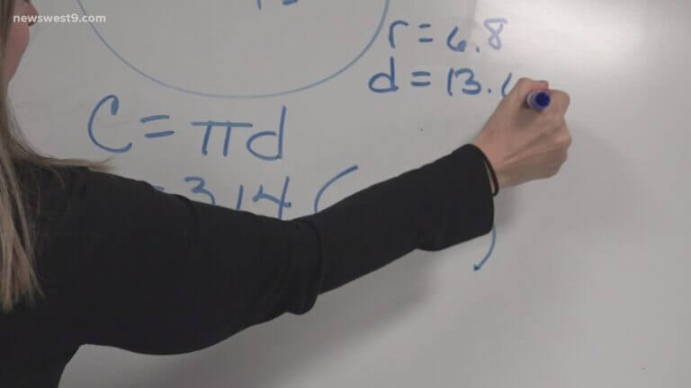 A teacher writes math equations on a whiteboard.