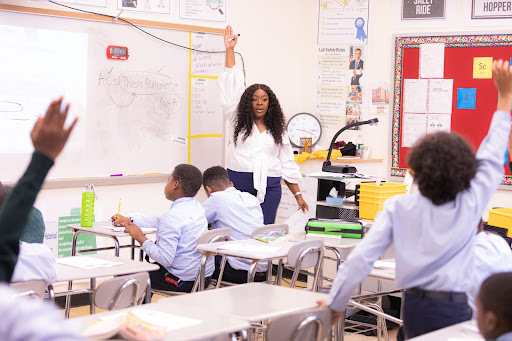 Kristen is standing in a classroom at the all-boys school she used to teach at. Students are raising their hands, eager to participate.
