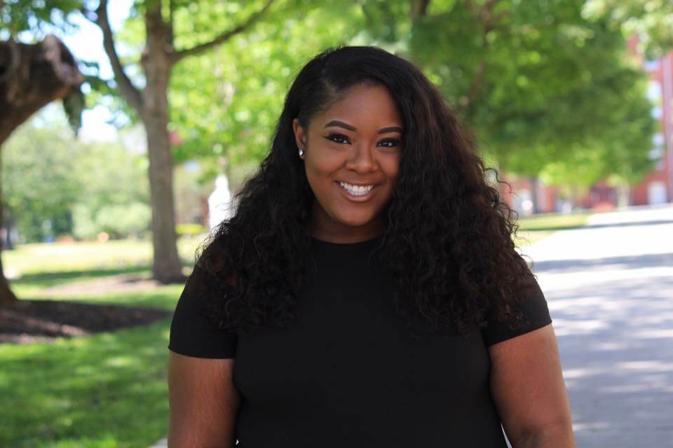 Kristen Gordon is standing outside, looking at the camera with a big, friendly smile. 