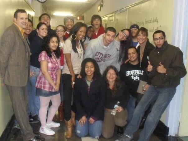 This is an old photo of Phellix with his high school classmates. They are huddled together in a school hallway. Phellix is in the center wearing a Gettysburg college hoodie. 