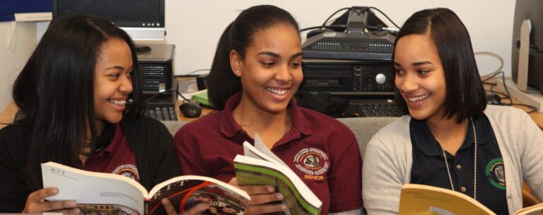 Three students are sitting together while looking at college materials. They look happy and excited as they talk with each other.