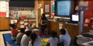 Janet is sitting in a circle with elementary aged students.