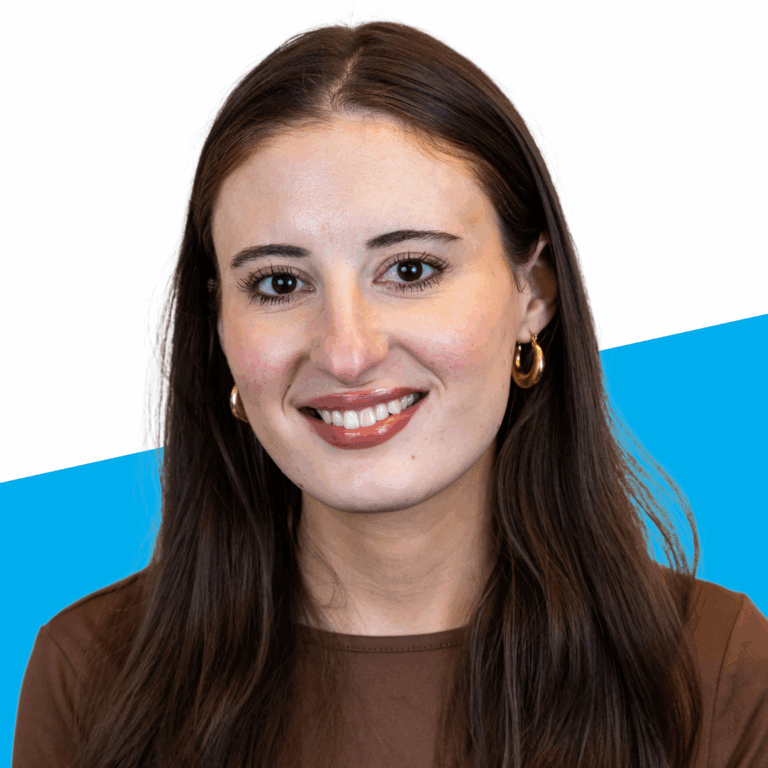 A woman with long brown hair, wearing gold hoop earrings and a brown top, smiles at the camera against a white and blue background, representing Student Leadership Network staff.