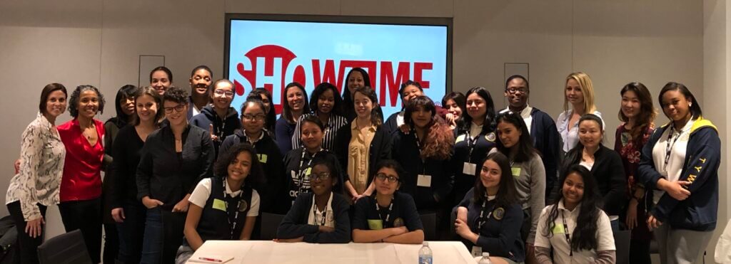 A big group of Showtime volunteers and TYWLS students pose for a group picture in front of a Showtime sign.