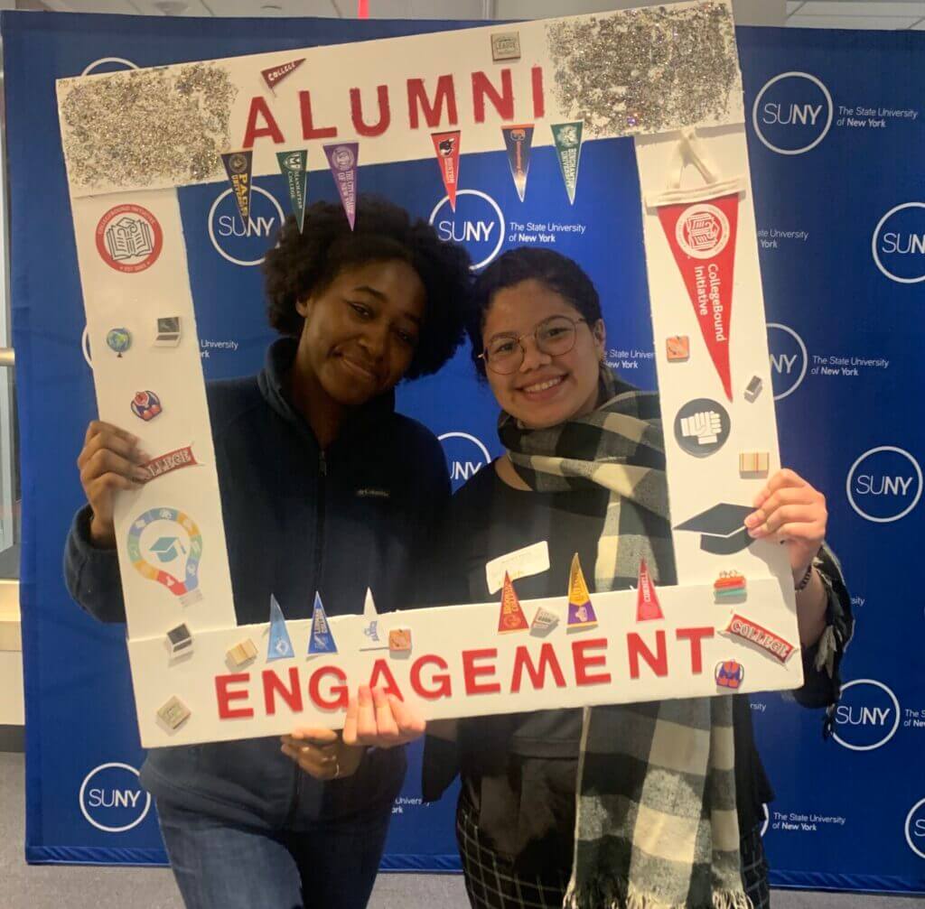 Sympoisum attendees pose for a picture with an Alumni Engagement frame.