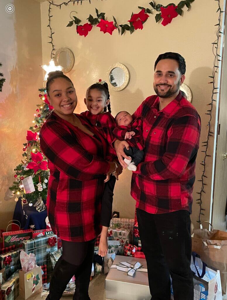Carolyn, Angel, and their two small children take a photo in front of their Christmas tree. 