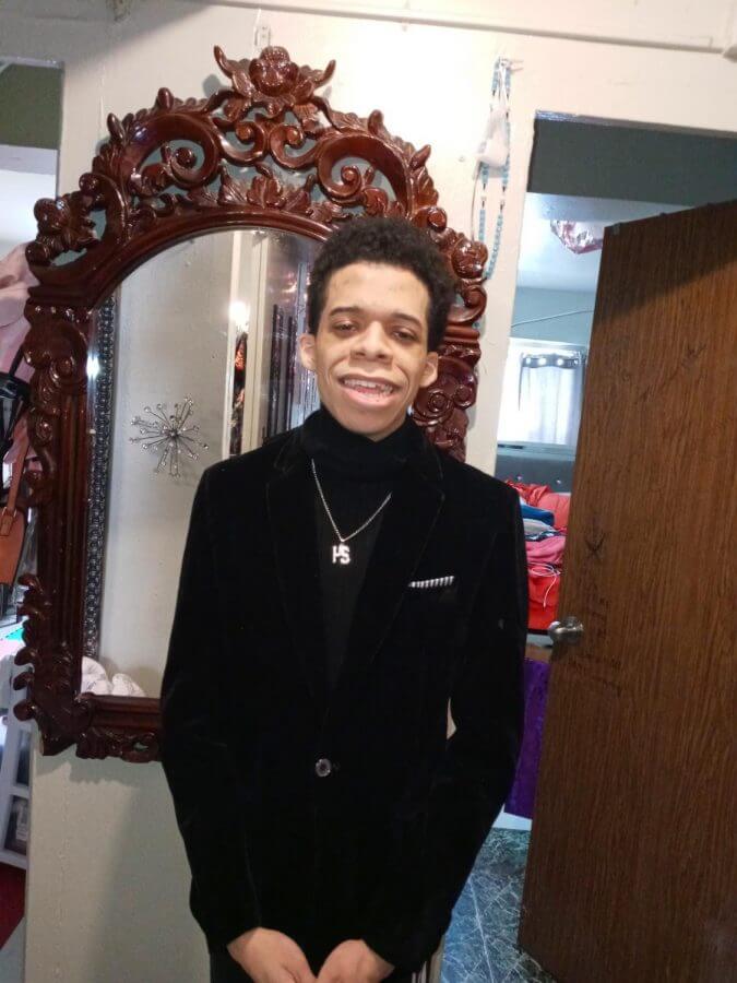 Javier stands in front of a mirror. He is wearing a dapper suit and smiling at the camera. 