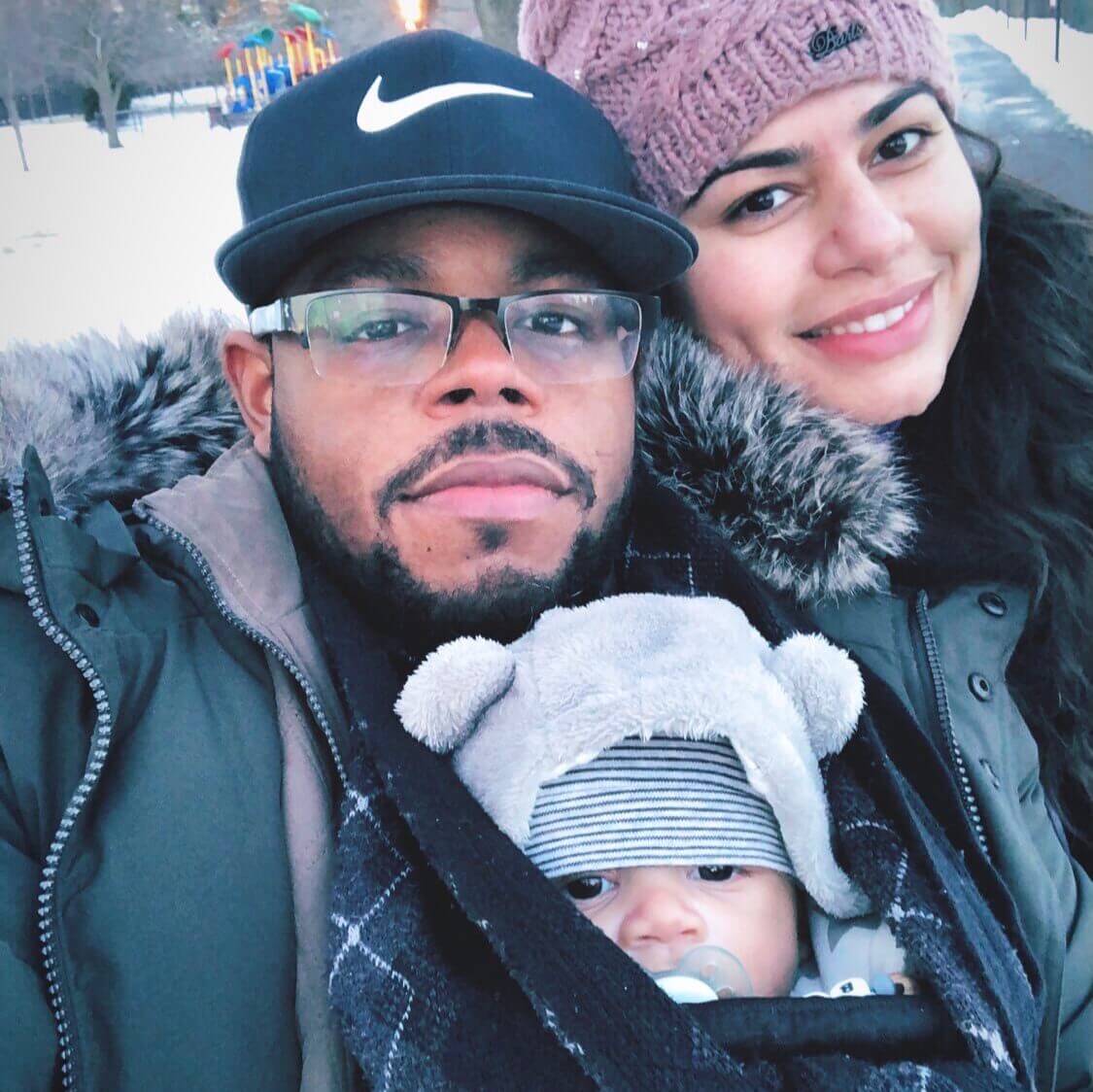 Eric with his fiance, Giselle, and their son. They are at a park on a winter day and there's snow on the ground. 