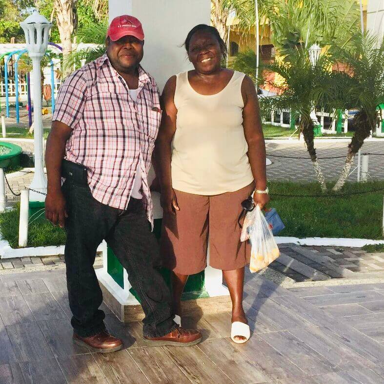 Eric's parents stand outside on sunny day and smile for the camera. They look relaxed and there are palm trees in the background. 