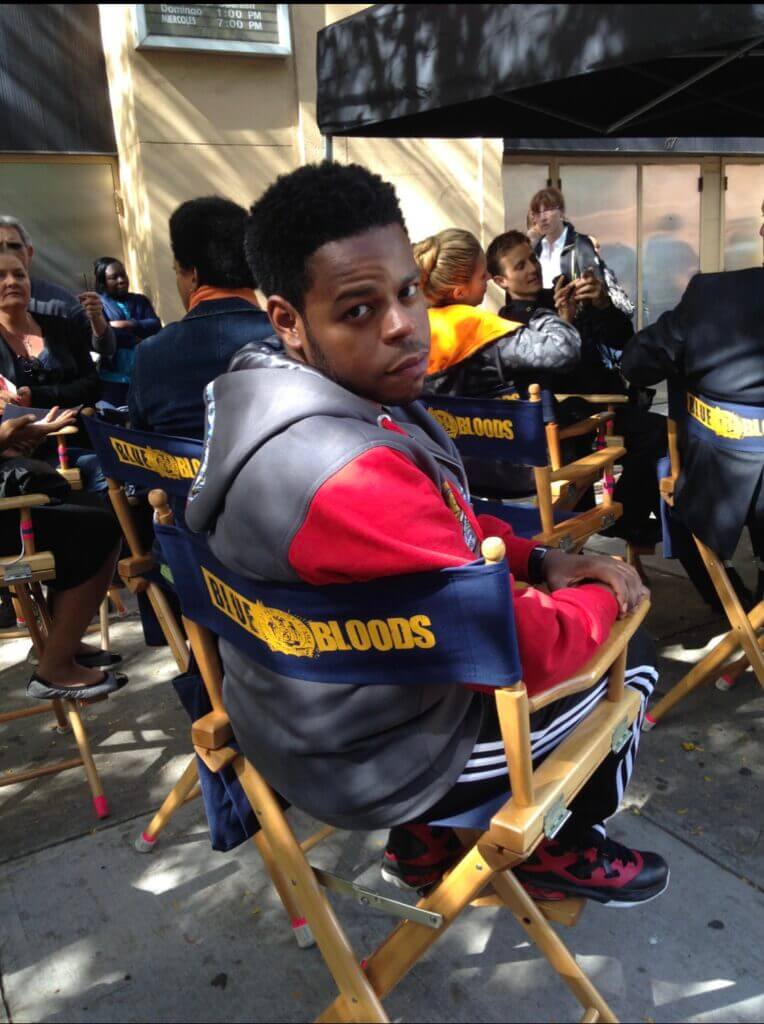 Eric Arriola sitting in an actor's chair on the set of Blue Bloods.