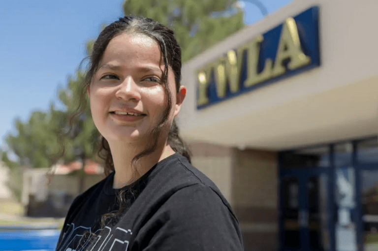 Ashley, a senior at Young Women's Leadership Academy, stands in front of the school and looks away from the camera.