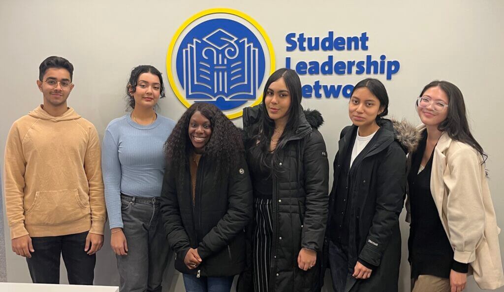 Janna is in the middle of a group of college students. They are hanging out in front of the SL Network office.