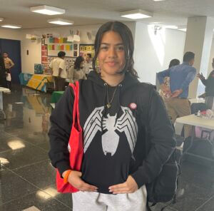 Dilenny stands with her hands in her front hoodie pocket and carrying a red tote bag.