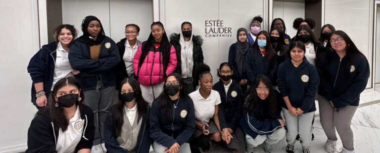 A group of TYWLS EH 10th graders poses in front of the Estee Lauder Companies logo at the GM Building