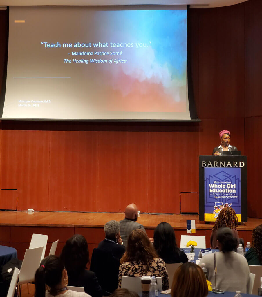 Dr. Monique Couvson on stage with quote "Teach me about what teaches you" on screen