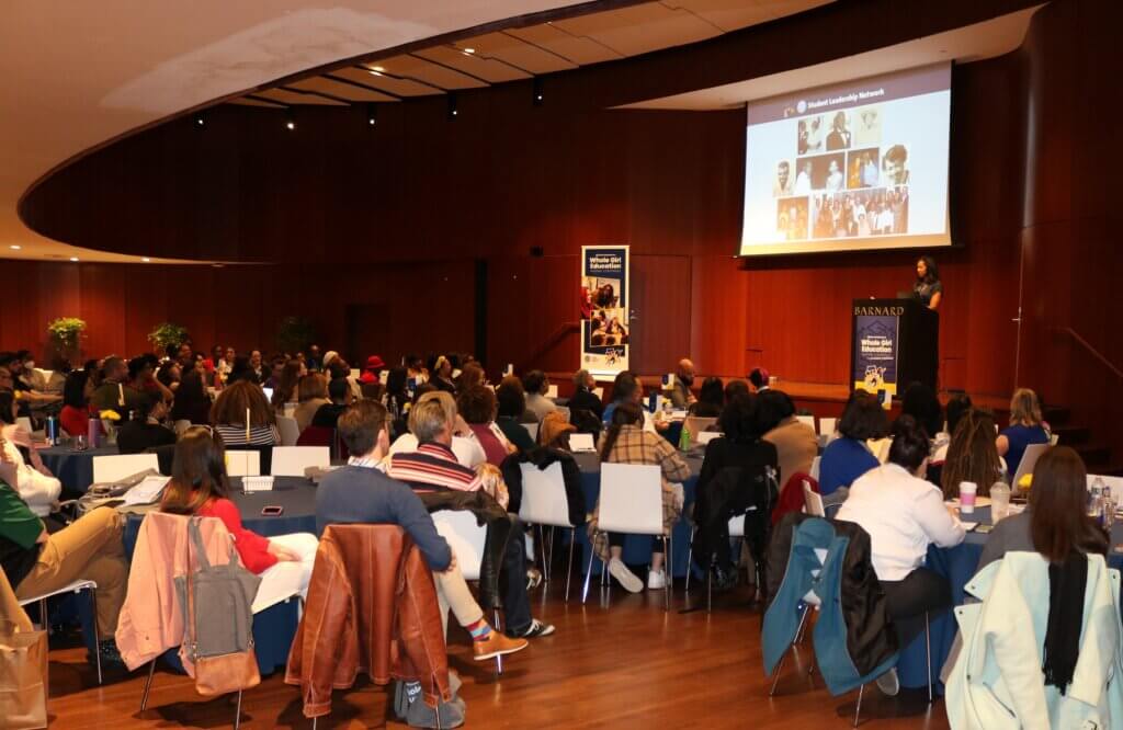 Yolonda Marshall on stage at the Whole Girl Education National Conference in front of a large crowd; pictures of her family on the screen