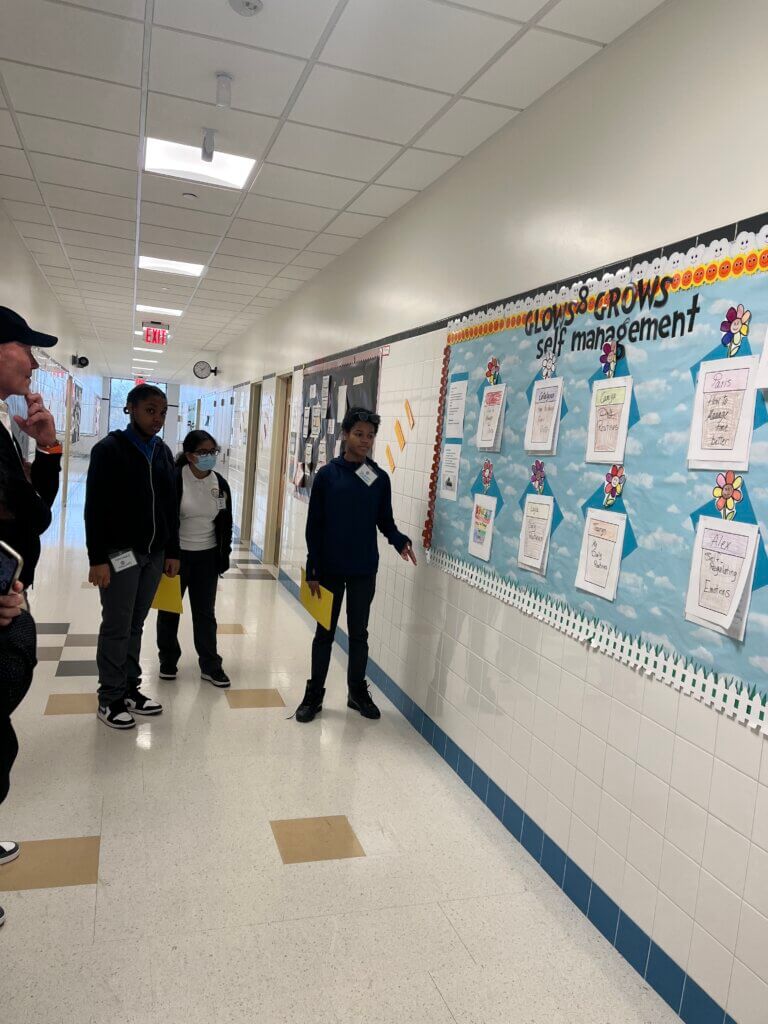 Students share their "Glows & Grows" bulletin board with volunteers.