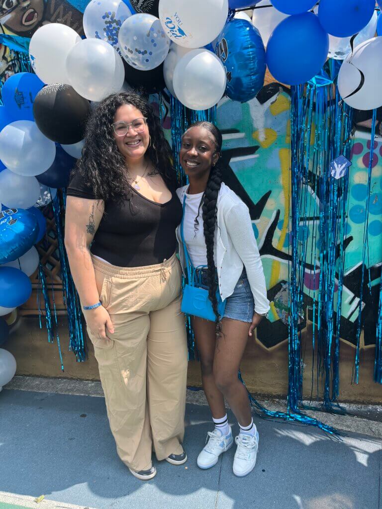 Joy poses smiling next to her director of college counseling under a balloon arch