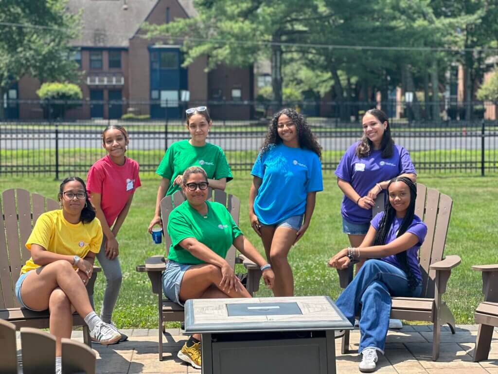 A director of college counseling and six students gather on a college campus lawn.