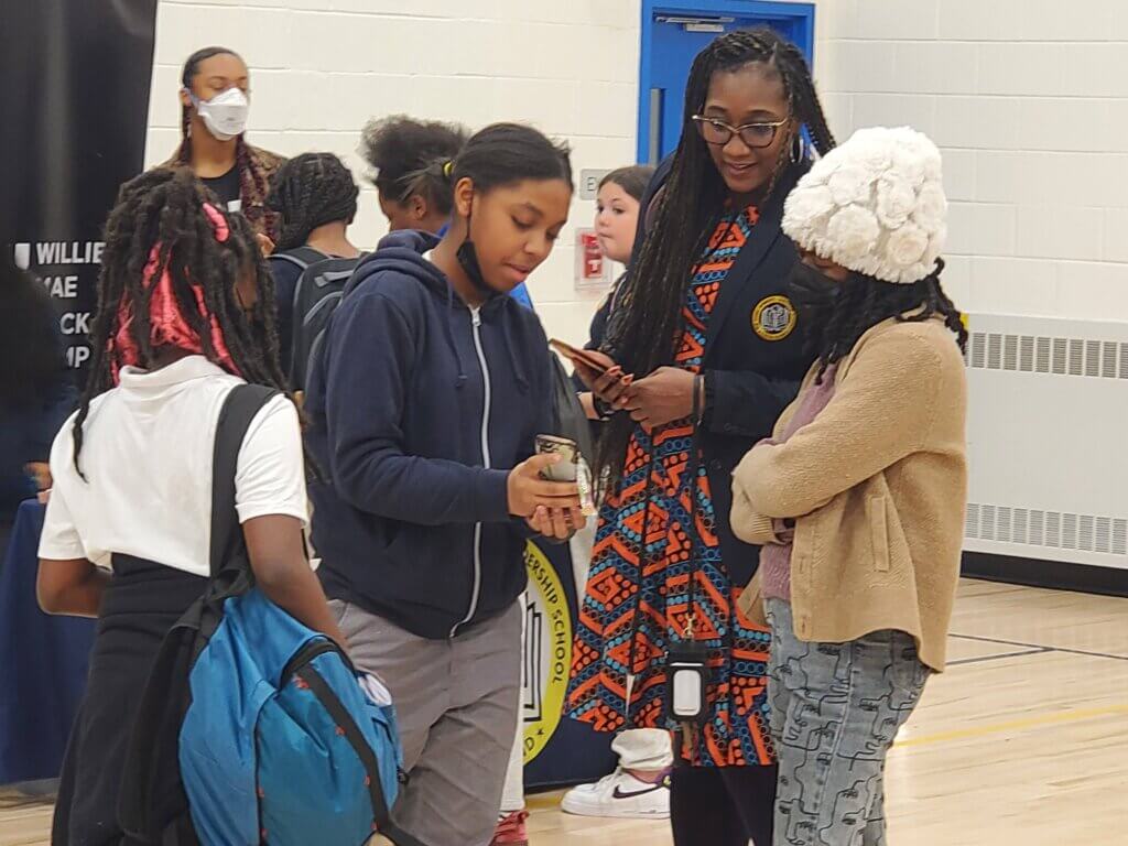 Principal Aisha Shepard and two students look at a student's phone together.