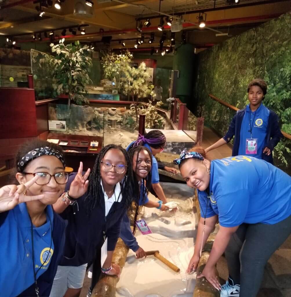 Group of girls explore sand in a science exhibit at a museum.