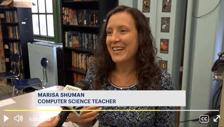 Computer science teacher Marisa Shuman talks into microphone.