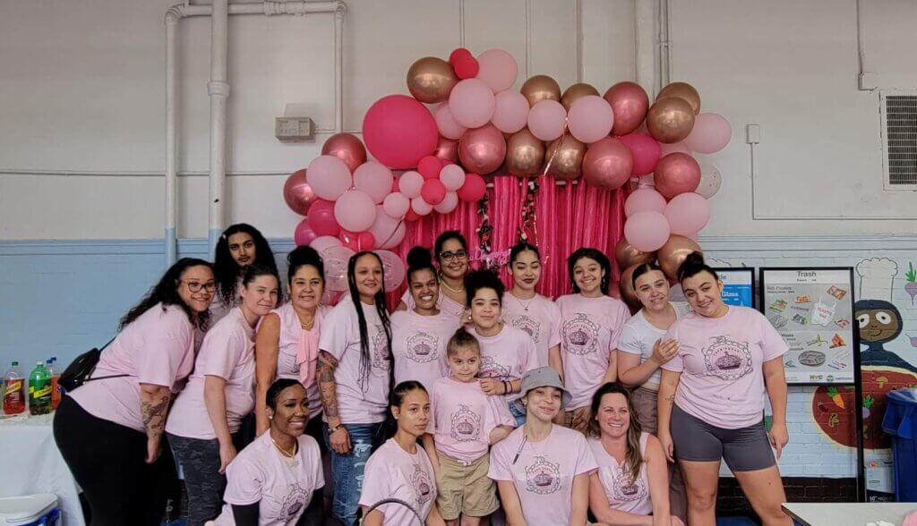 Group of students and adult volunteers in pink shirts pose in front of balloons for Prom Squad event