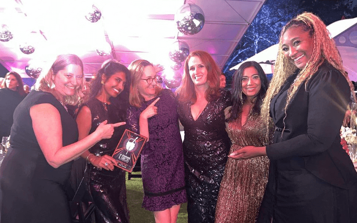 Six female school principals in formal wear point to the principal in the middle, Devon Eisenberg, who won an award at the event.