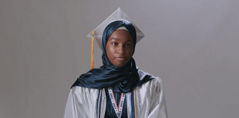 Student in headscarf, graduation cap, and gown wears a medal on ribbon around her neck