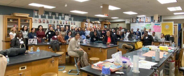 Over 40 adult volunteers and students in a science lab, some seated and some standing.