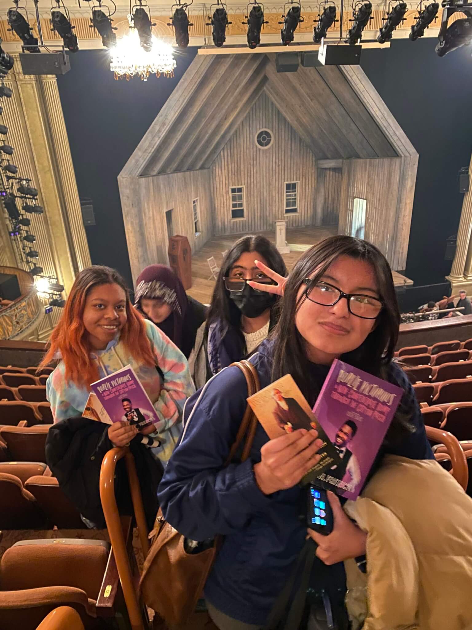 Four students hold up Broadway play booklet for Purlie Victorious inside a theater
