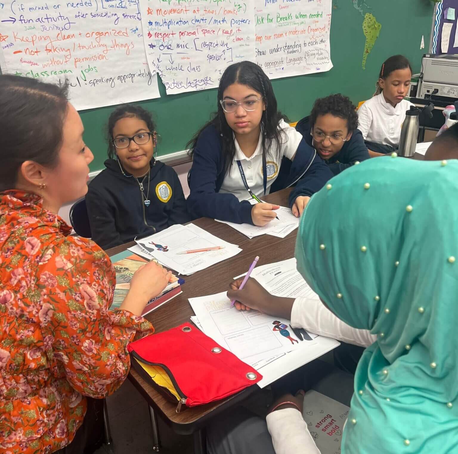 Five students take notes around a desk with an adult volunteer seated next to them