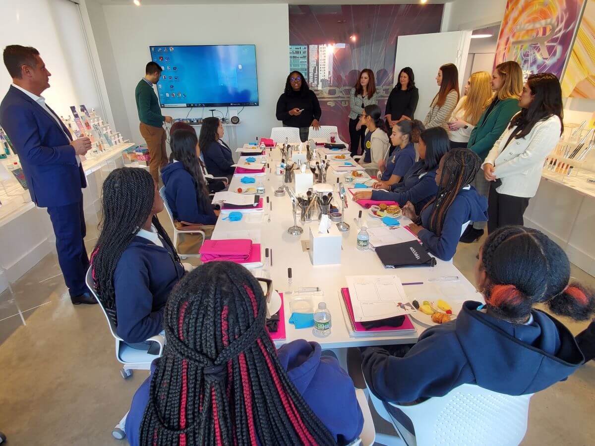 Students sit at an oval table while staff from Intercos and Student Leadership Network stand and introduce the day's agenda.