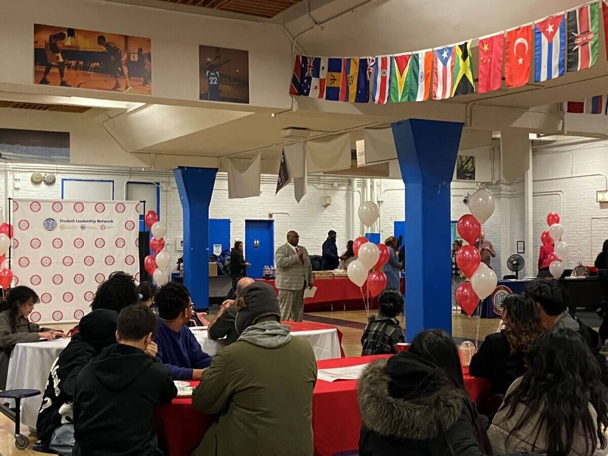 Staff member stand with microphone to talk to seated students in cafeteria.