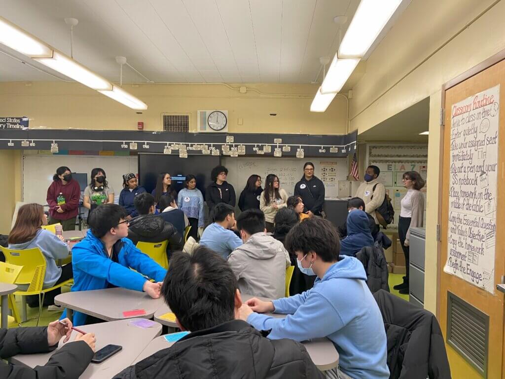 Ten alumni at front of classroom speak with group of seated students