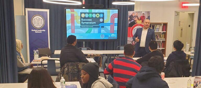 "Future Success Symposium" graphic on screen at front of room, with alumni and students seated facing the speaker