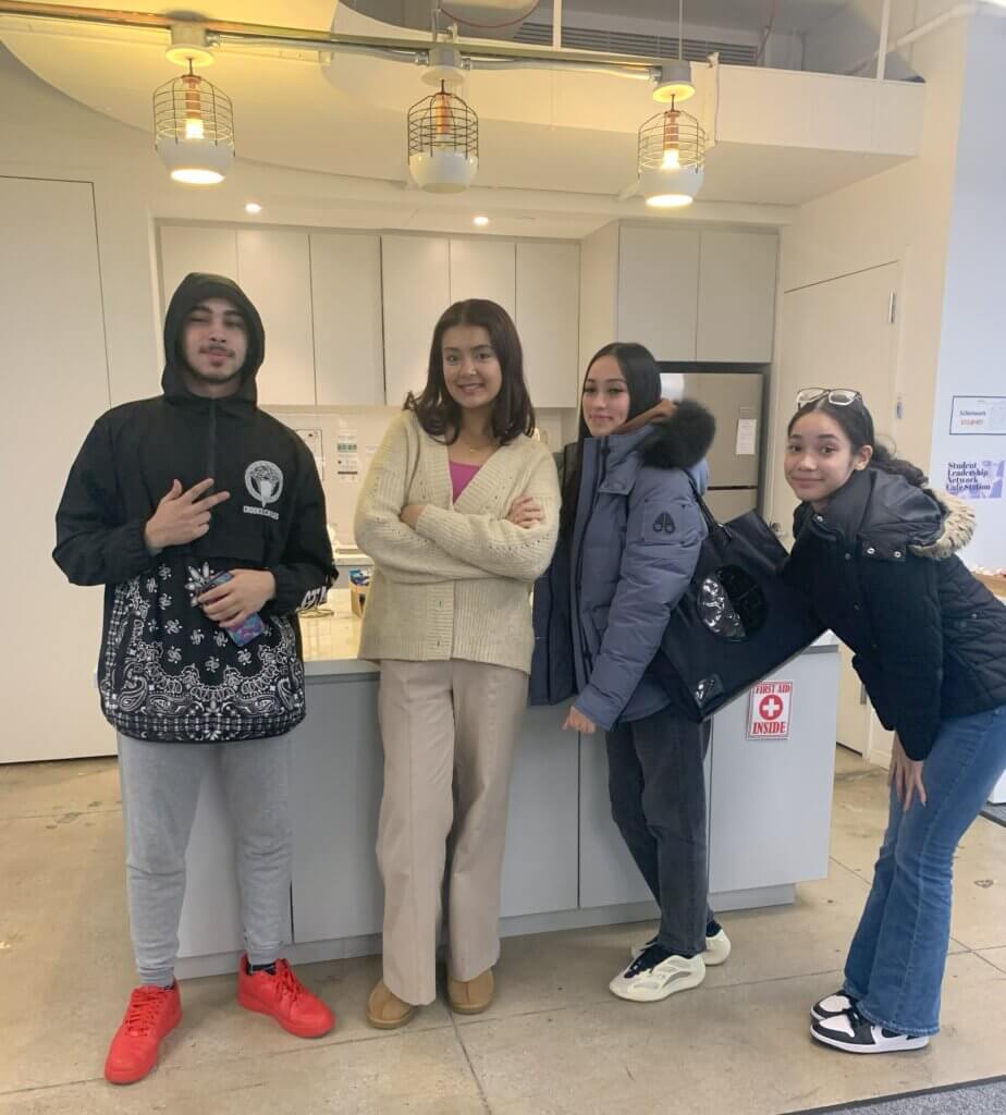 A young man and three young women in sweaters and jackets gather in front of a marble table.