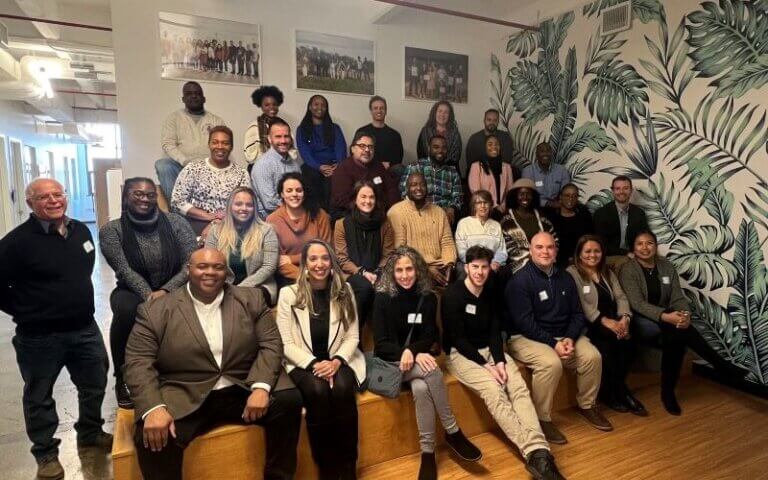 Nearly 30 leaders in the education and workforce development sector are seated on four rows of an ascending bench