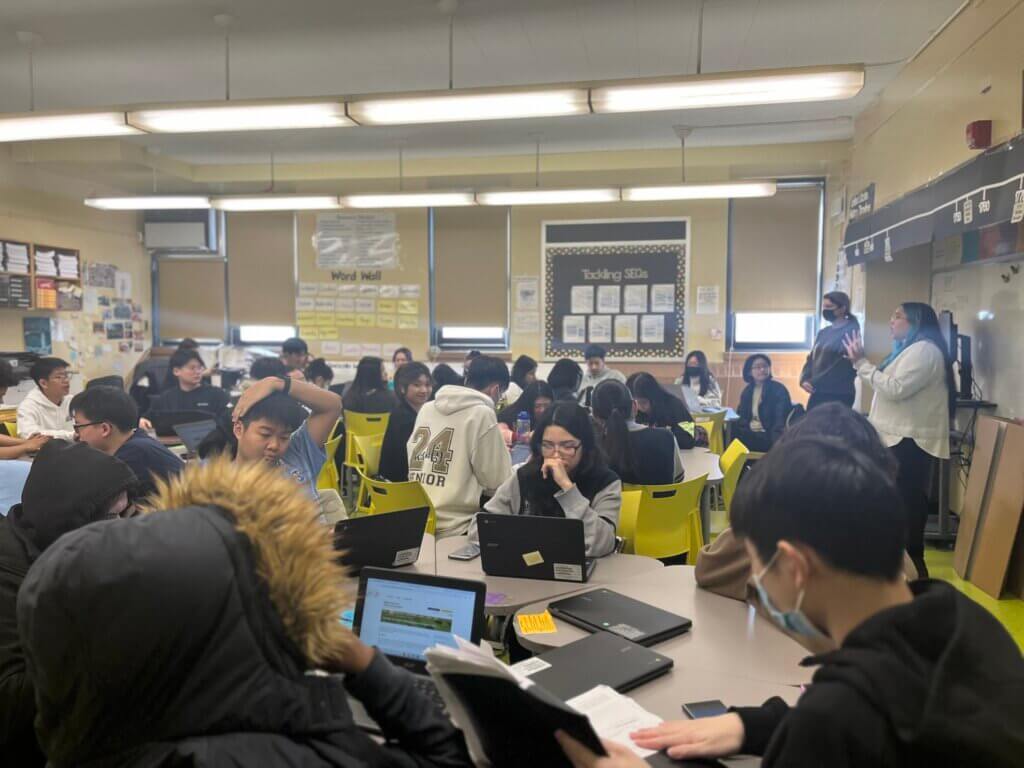 Students with laptops review online financial aid forms, with a director of college counseling guiding them from the front of the room.