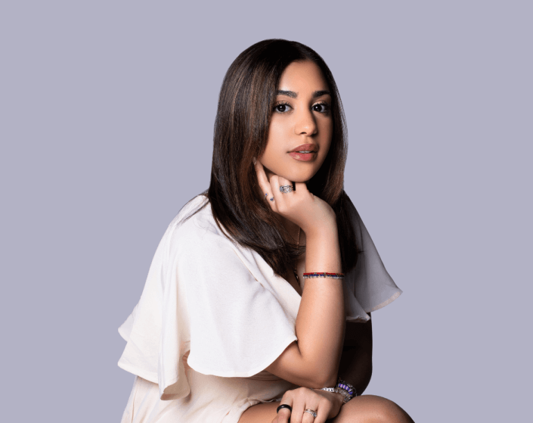 Young woman is seated, with chin resting on her hand, wearing colorful bracelets and rings on her hands