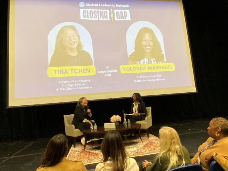 Tina Tchen and Yolonda Marshall are seated on stage holding microphones, while audience looks on.