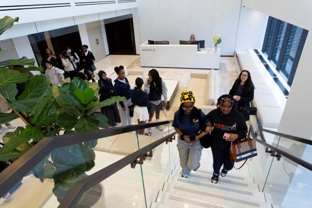 Students walk up a staircase in a brightly lit office atrium with plants on the left side