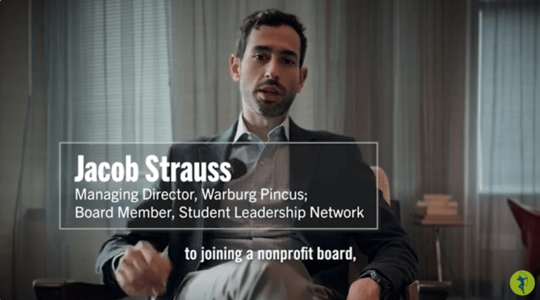 Man in suit speaks to camera, with his job and board affiliations as text on screen