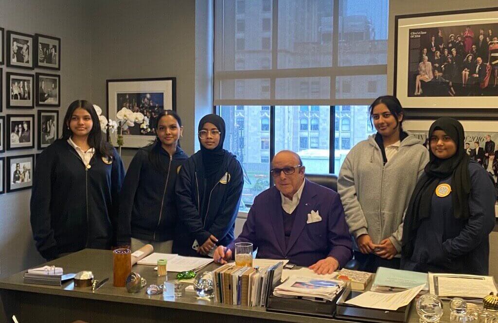 Students stand behind desk with music executive Clive Davis in an office setting