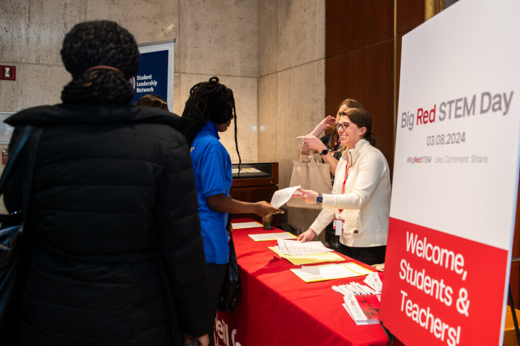 Students receive paperwork at a sign in desk with large sign "Big Red STEM Day" on the side