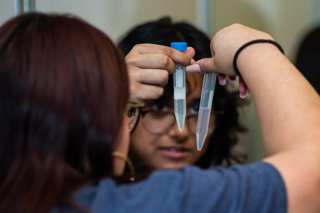 Two girls hold up plastic test tubes during a DNA lab