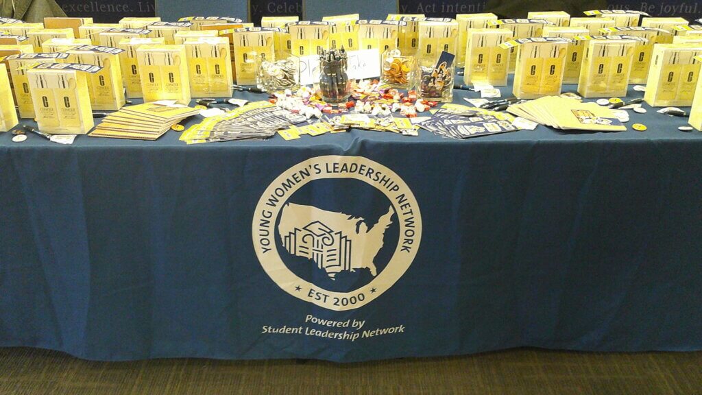 In-kind gifts for the conference include Clinique lotions, stickers, notebooks and more scattered across a table