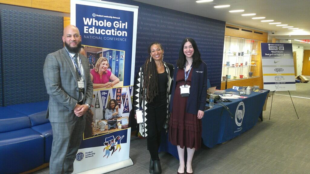 Jon Roure, Ruha Benjamin, and Sarah Boldin pose for photo in front of Whole Girl Education National Conference signage